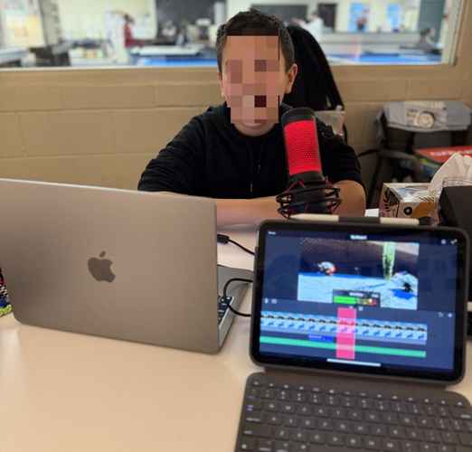 A Club member sitting behind a MacBook with a microphone in front of them. iPad in view, recording their audio.