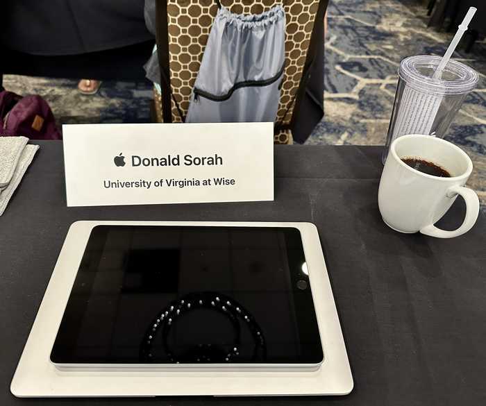 Desk with Apple Learning Academy resources including iPad, MacBook, coffee, and water cup.