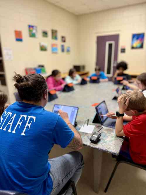 Teaching leading a class on their iPad with students following along around the table