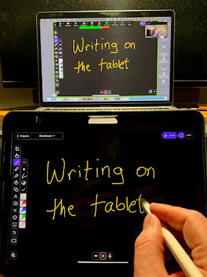 A hand writing letters on a digital whiteboard on a tablet. The writing appears in Zoom on the connected laptop