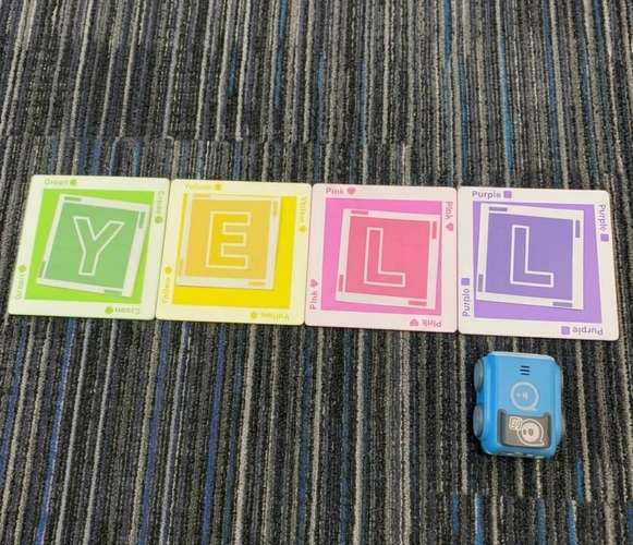A top-down view of four colorful letter cards spelling out "YELL" laid out in a row next to a small blue Sphero Indi robot on