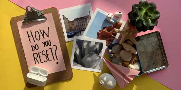 An image from above on a yellow and pink background with the text How do you reset? On a clipboard surrounded by items.