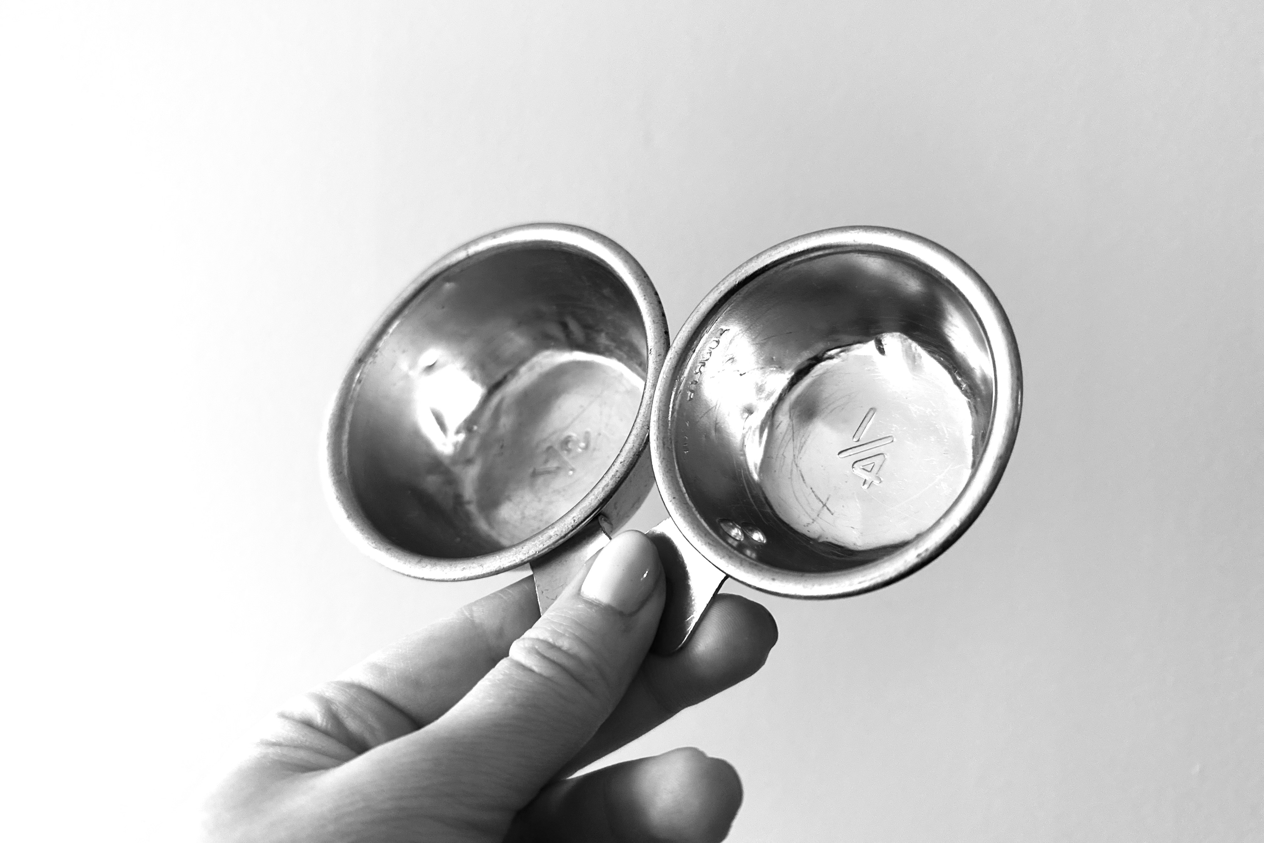 A hand holds up two vintage measuring cups by the handle.