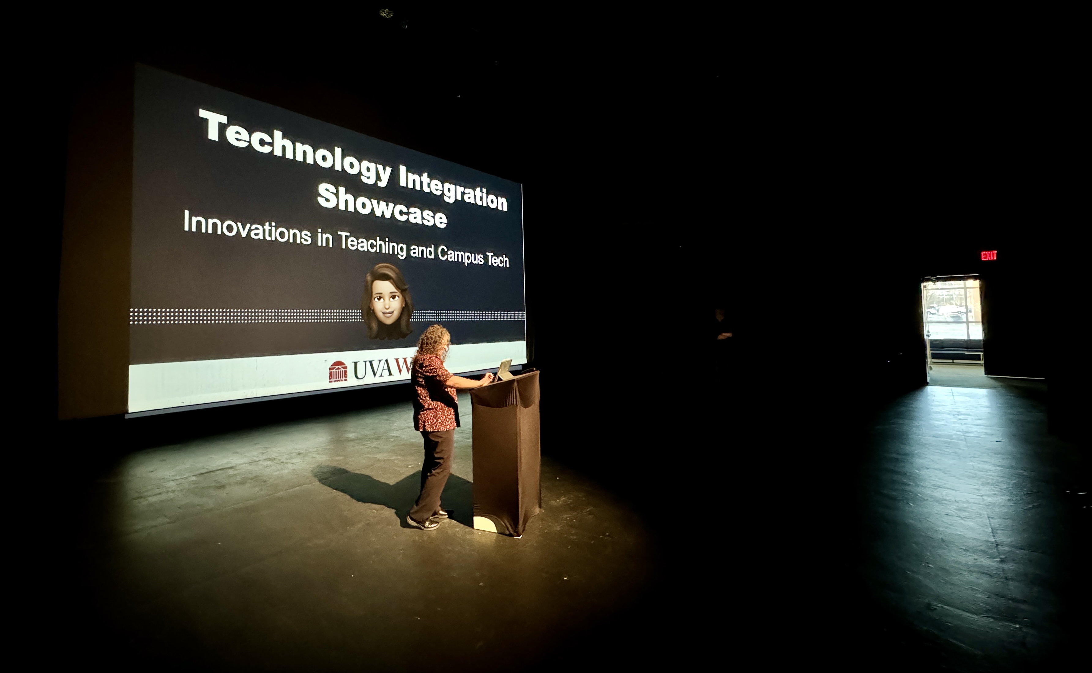 Presenter standing at a lectern with a large projector screen behind. Technology Innovation Showcase is displayed on screen.