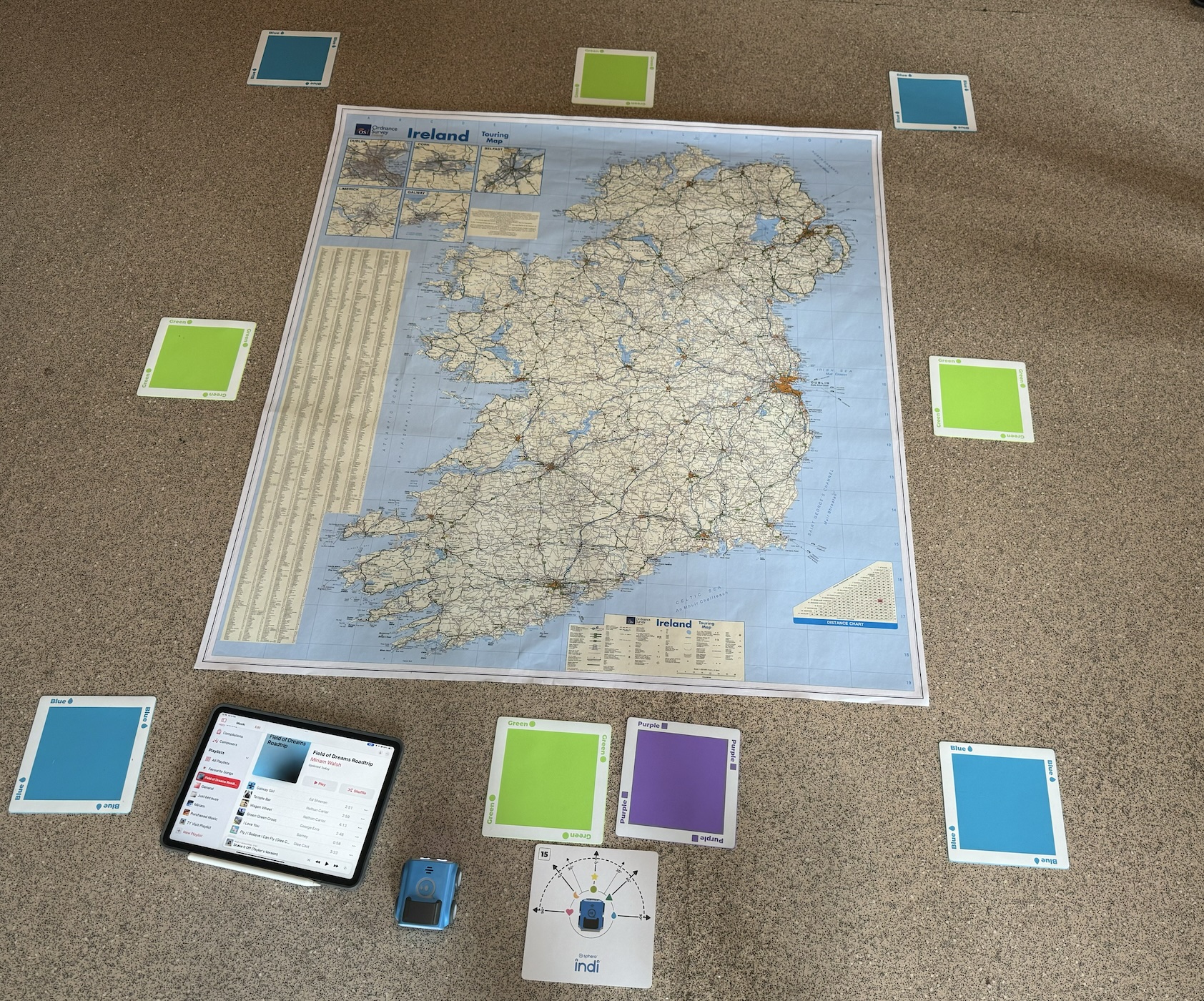Image of a map of Ireland on the floor, with an iPad showing an Apple Music Playlist and some Indi coding cars. 